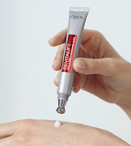 Eine Hand drueckt einen Tropfen Revitalift Filler HA aufpolsternde Pflege fuer das Auge auf den anderen Handruecken